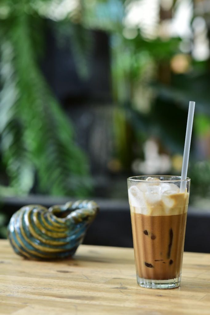 Glass of creamy iced coffee on a wooden table with lush garden background.
