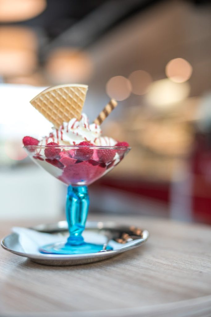 Close-up of a raspberry ice cream sundae in a glass cup with wafer decor.